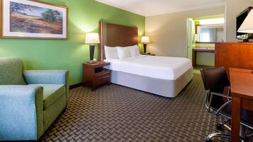 A hotel room with a bed, a chair, a desk, and a painting on the wall.