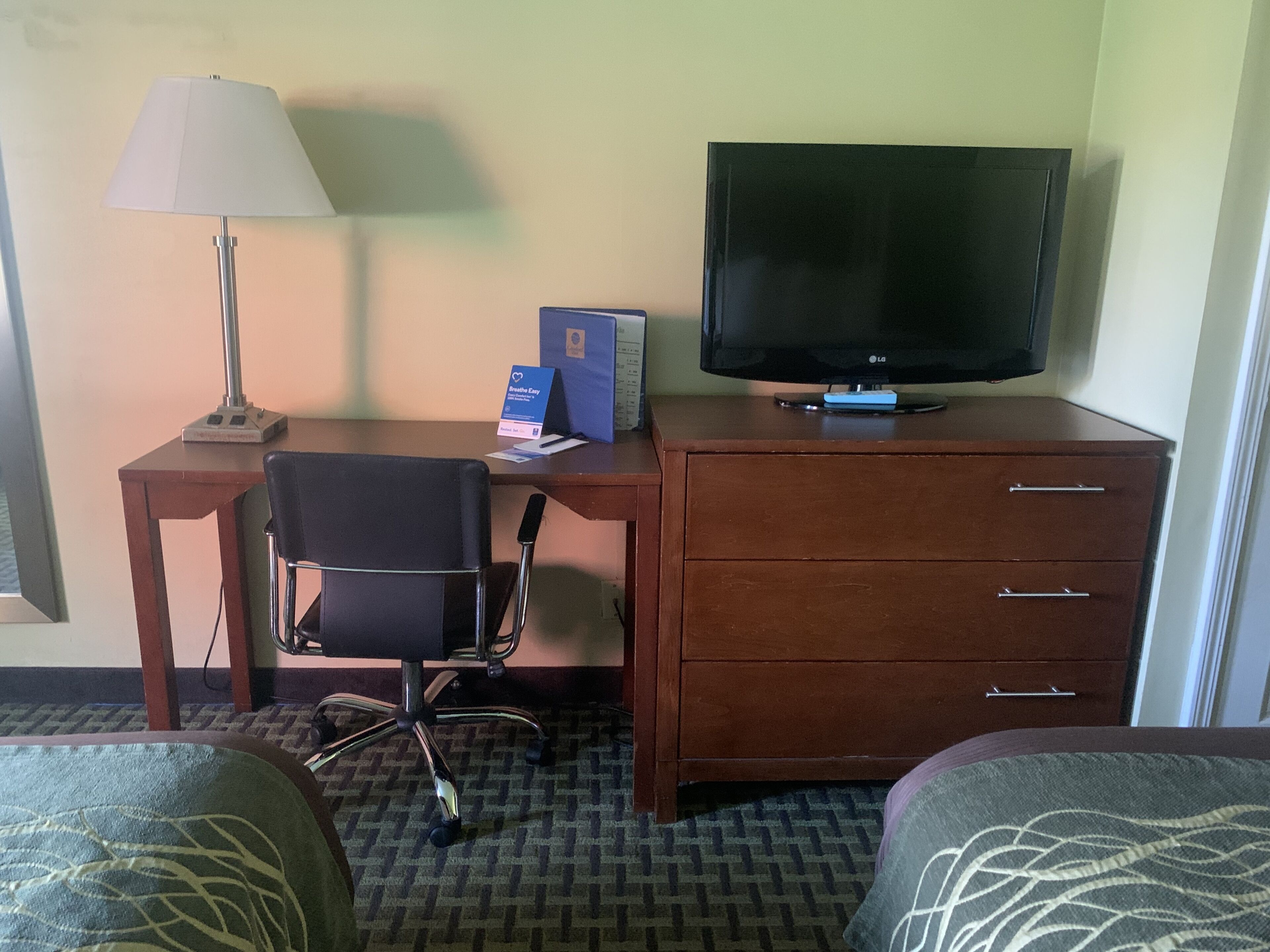 A hotel room with a desk, chair, television, and a bed.