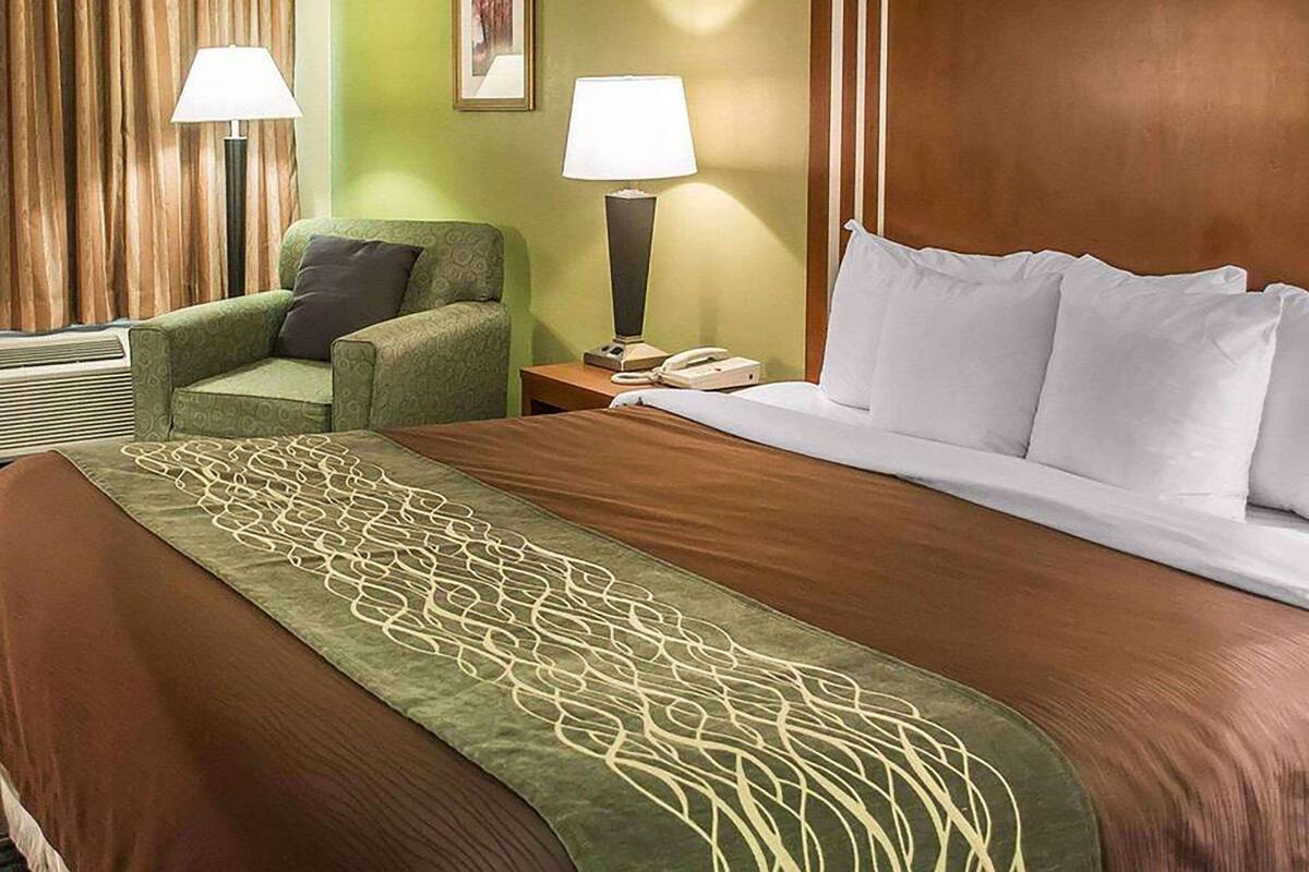 A hotel room with a large bed, a green armchair, two bedside lamps, a telephone, and a wall-mounted picture.