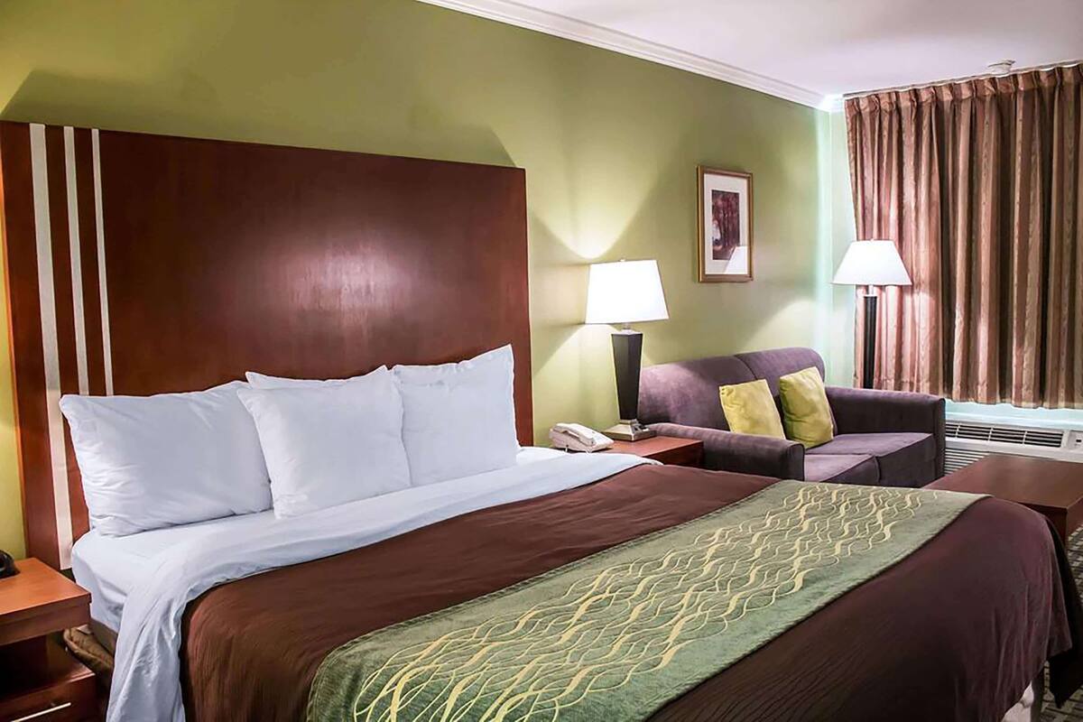 A hotel room with a large bed, a chair, a desk, and a lamp.