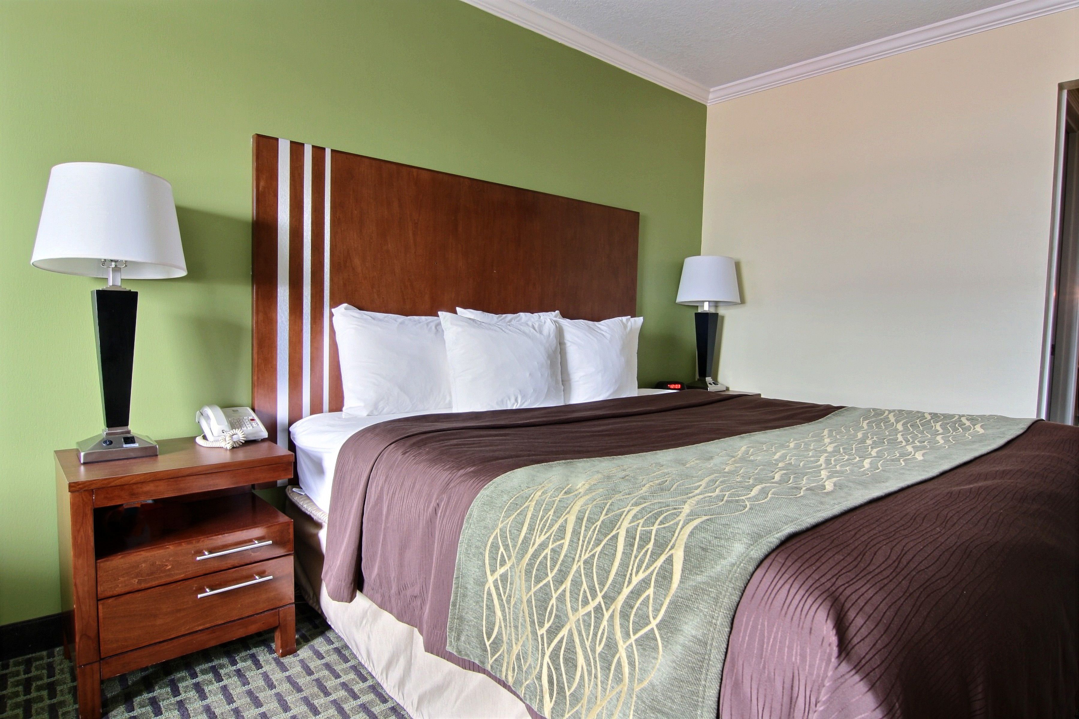 A hotel room with a large bed, two bedside tables with lamps, a wooden headboard, and a green wall.