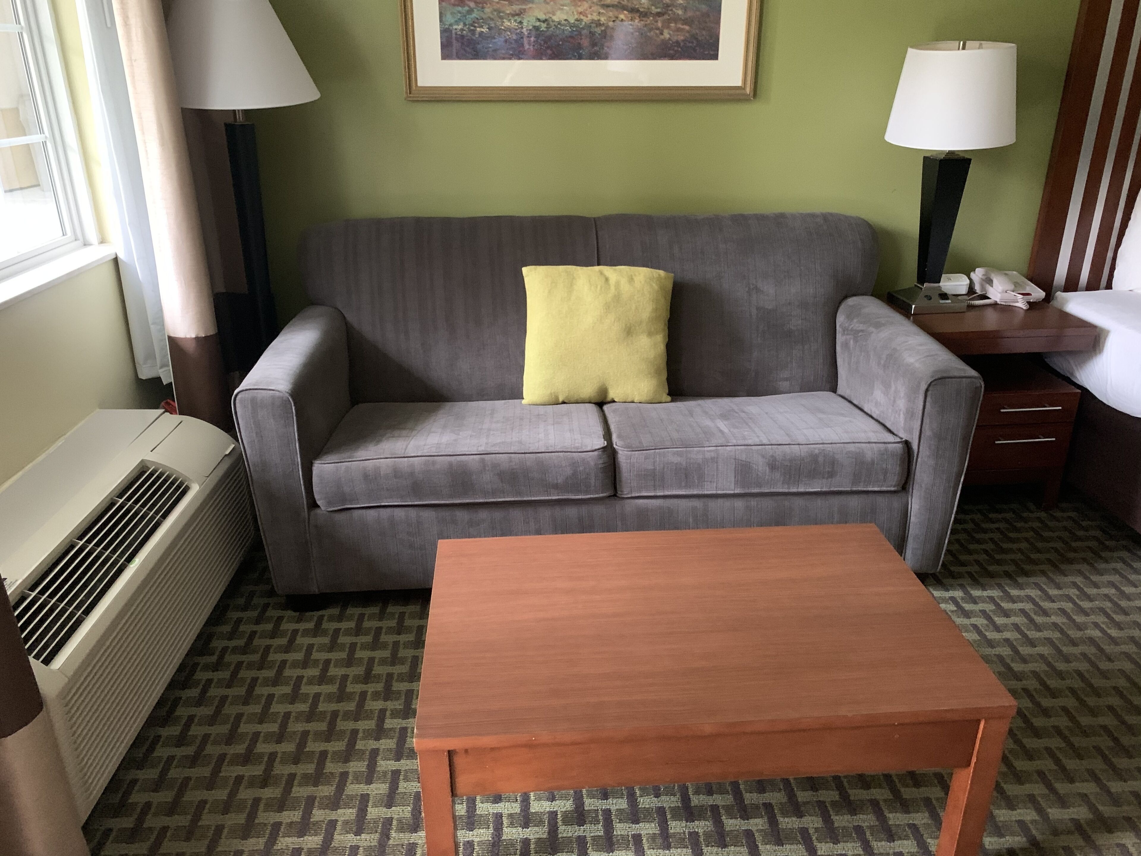 A room with a grey sofa, a wooden table, a standing heater, and a framed picture on the wall.