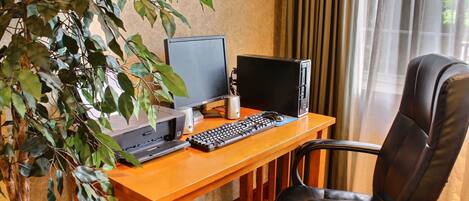 Un escritorio de madera con una computadora, que incluye un monitor, teclado y ratón. Hay una silla de cuero negro y una planta en maceta.