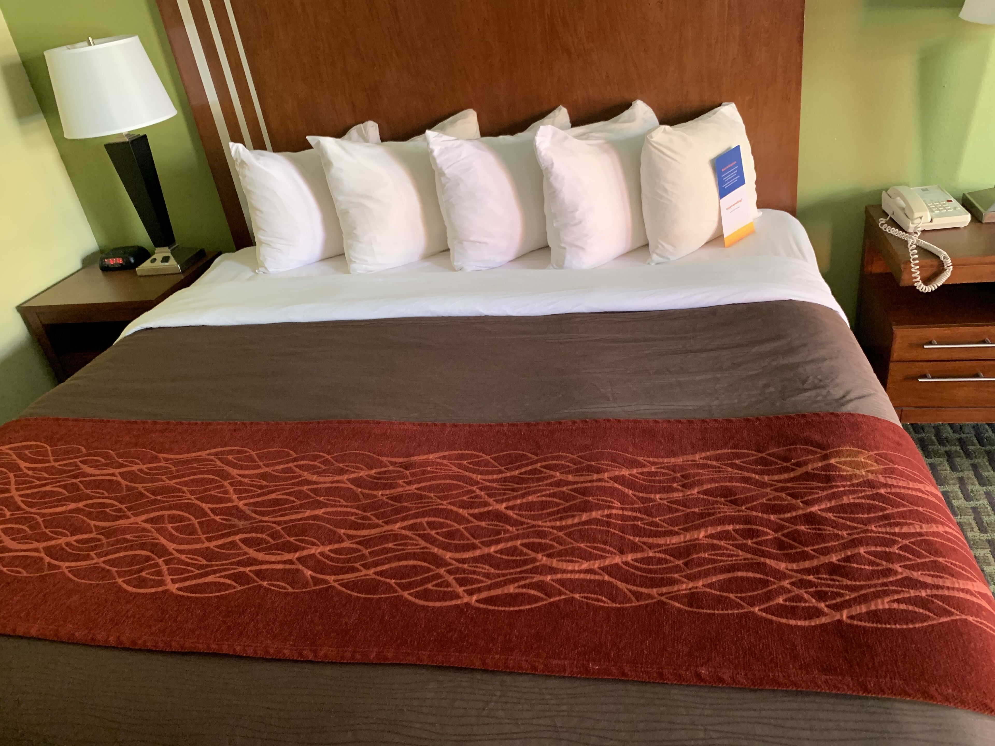 A hotel room with a bed, a nightstand with a lamp, a phone, and a bedside table.