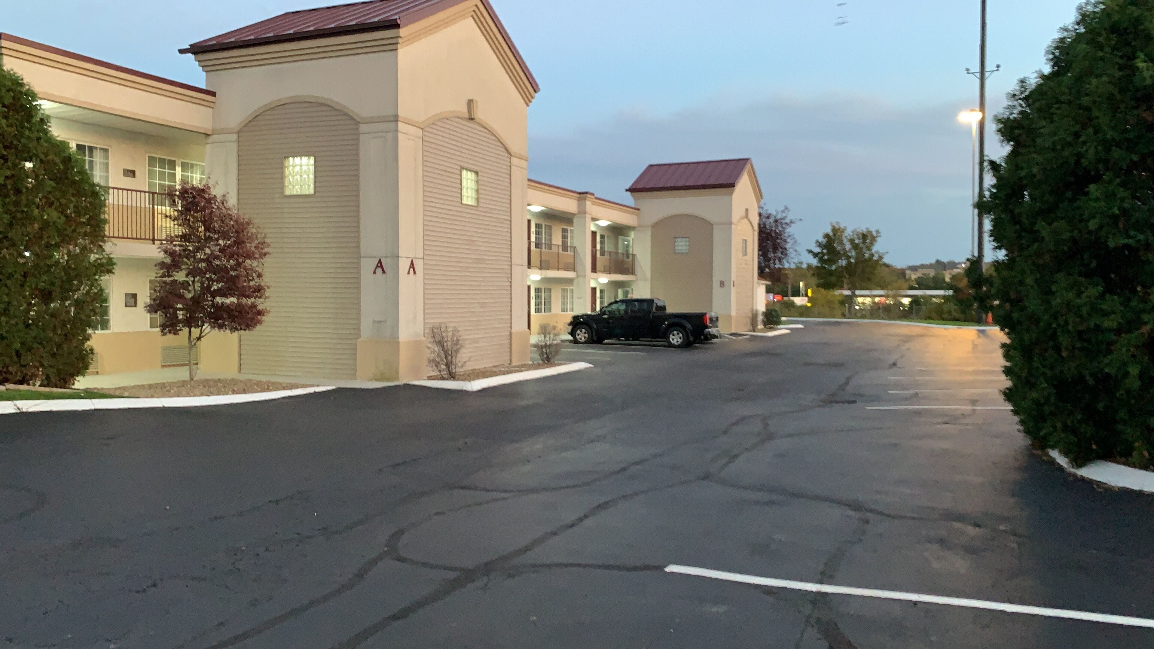 A parking lot with a black pickup truck parked in front of a building with a beige facade and a red roof.