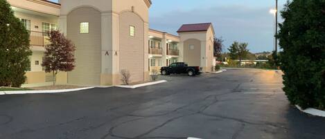 A parking lot with a black pickup truck parked in front of a building with a beige facade and a red roof.