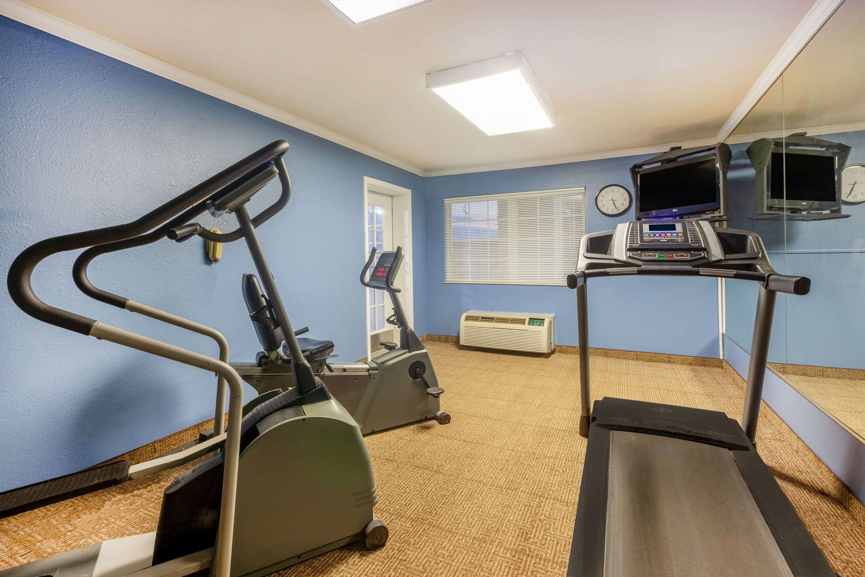 A fitness room with exercise equipment, a treadmill, and a mirrored wall.