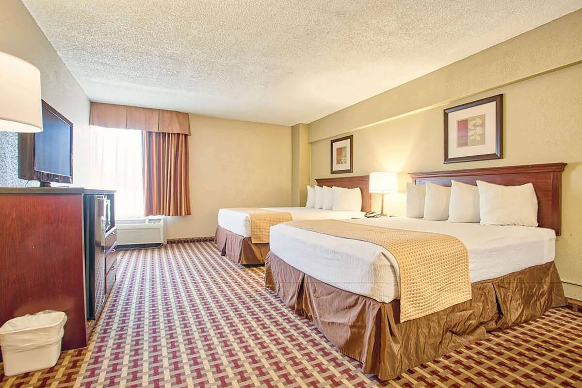 Habitación de hotel con dos camas, un escritorio con lámpara, televisión y aire acondicionado.