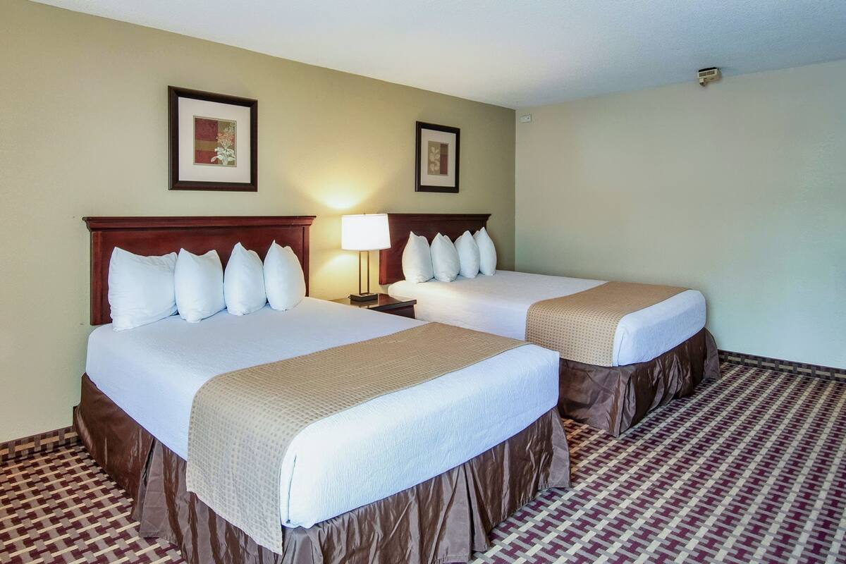 Habitación de hotel con dos camas, piso estampado y cuadros en las paredes.