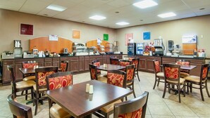 Un comedor de hotel con varias mesas y sillas, un mostrador de buffet y distintas estaciones de comida y bebidas.