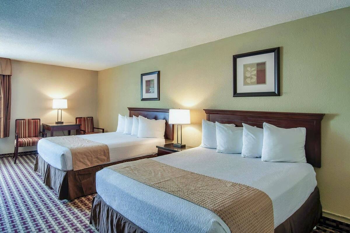 A hotel room with two beds, a desk, chairs, and lamps.