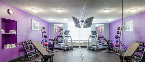 A gym with purple walls, treadmills, dumbbells, and exercise balls.
