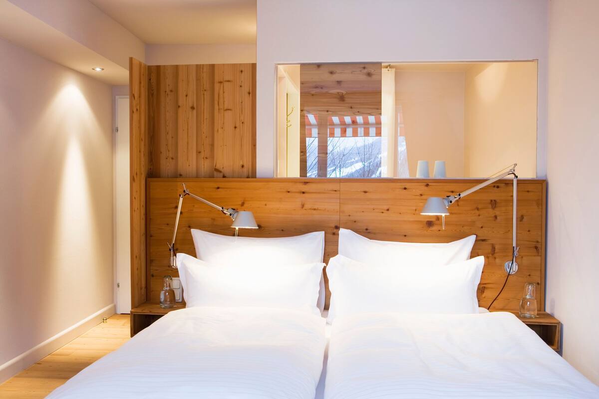 Cama doble con ropa de cama blanca, cabecera de madera, lámparas de noche y un espejo sobre la cama.