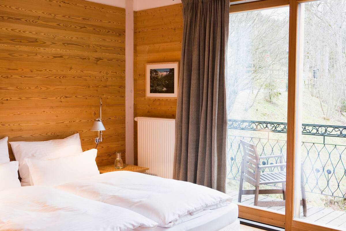 Un dormitorio con paneles de madera, una cama grande, una mesita de noche, una lámpara y un cuadro en la pared.