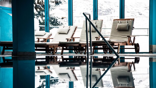 Zona de piscina con sillones de descanso y vistas a montañas nevadas a través de amplios ventanales.