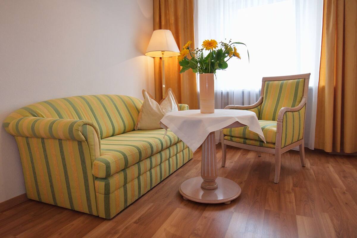 A room with a striped sofa, a chair, a table with a vase of flowers, and a lamp.