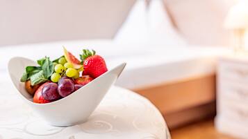A bowl of fruit on a white pillow with a bed and a nightstand in the background.