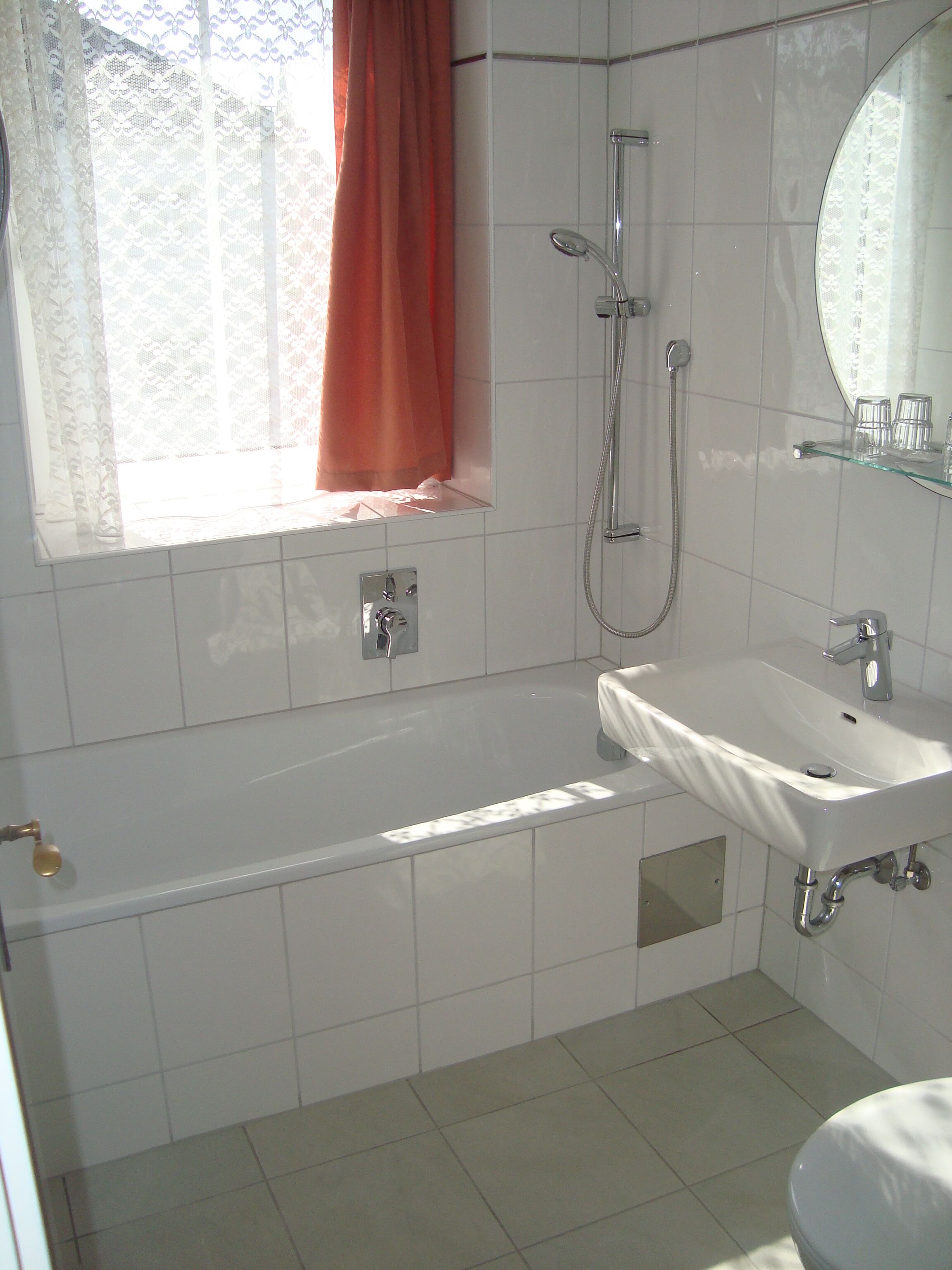 A bathroom with a bathtub, a sink, a shower, and a window with curtains.