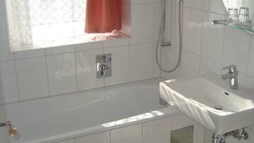 A bathroom with a bathtub, a sink, a shower, and a window with curtains.