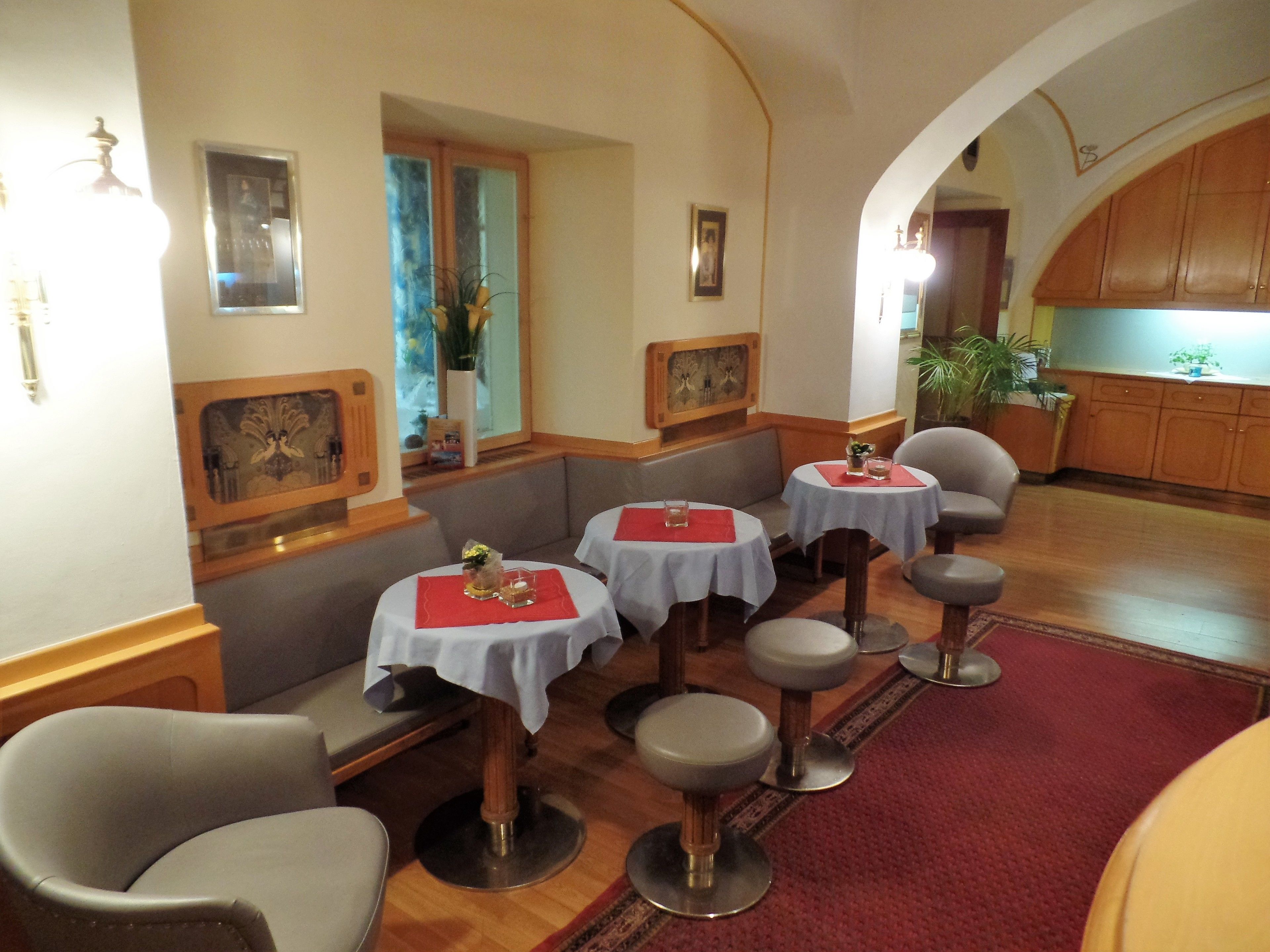 A restaurant with booths and round tables, wooden flooring, and a red carpet.