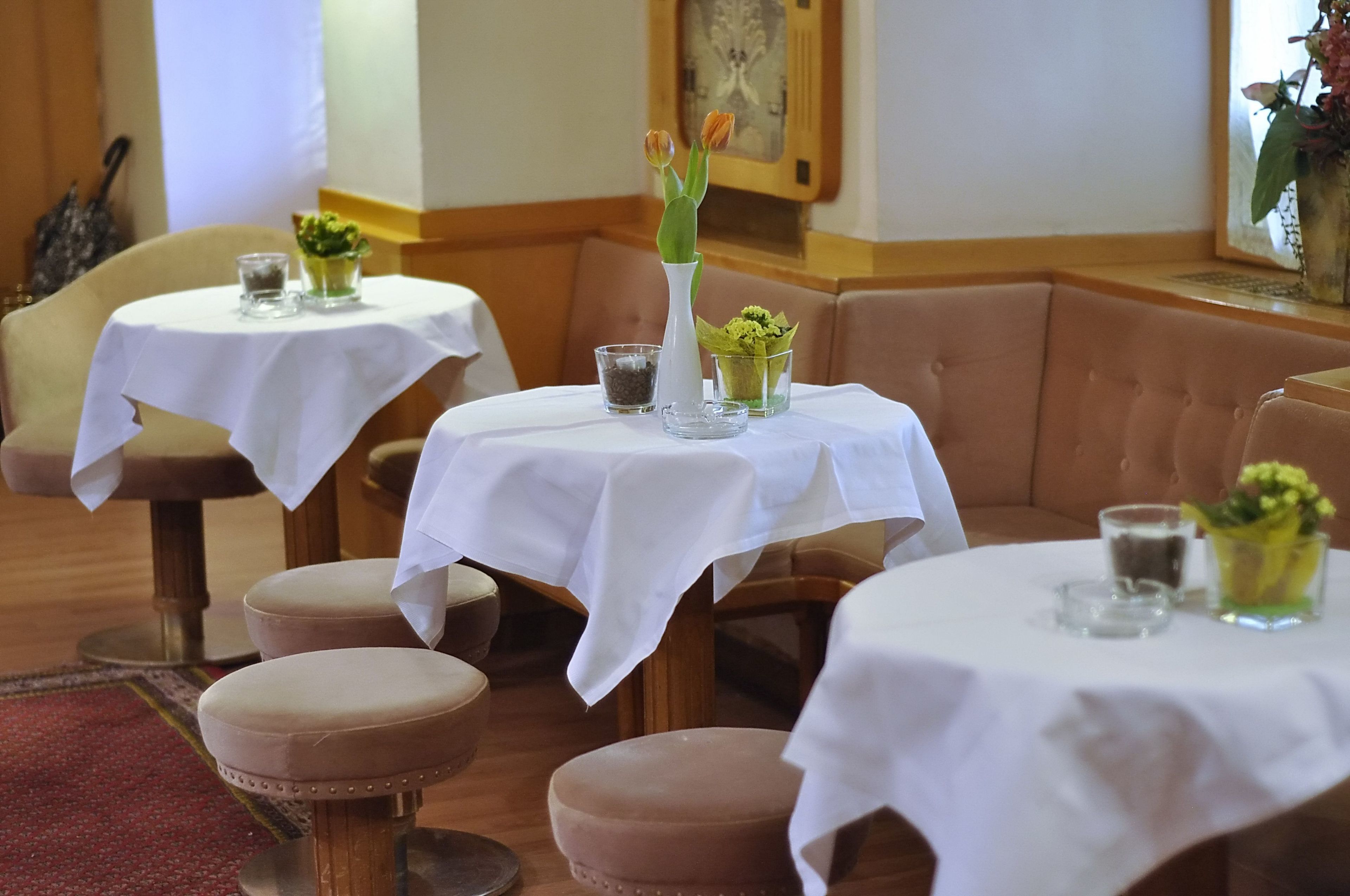 Un espace repas avec des tables recouvertes de nappes blanches, chacune agrémentée d’un petit vase de fleurs et d’un verre.
