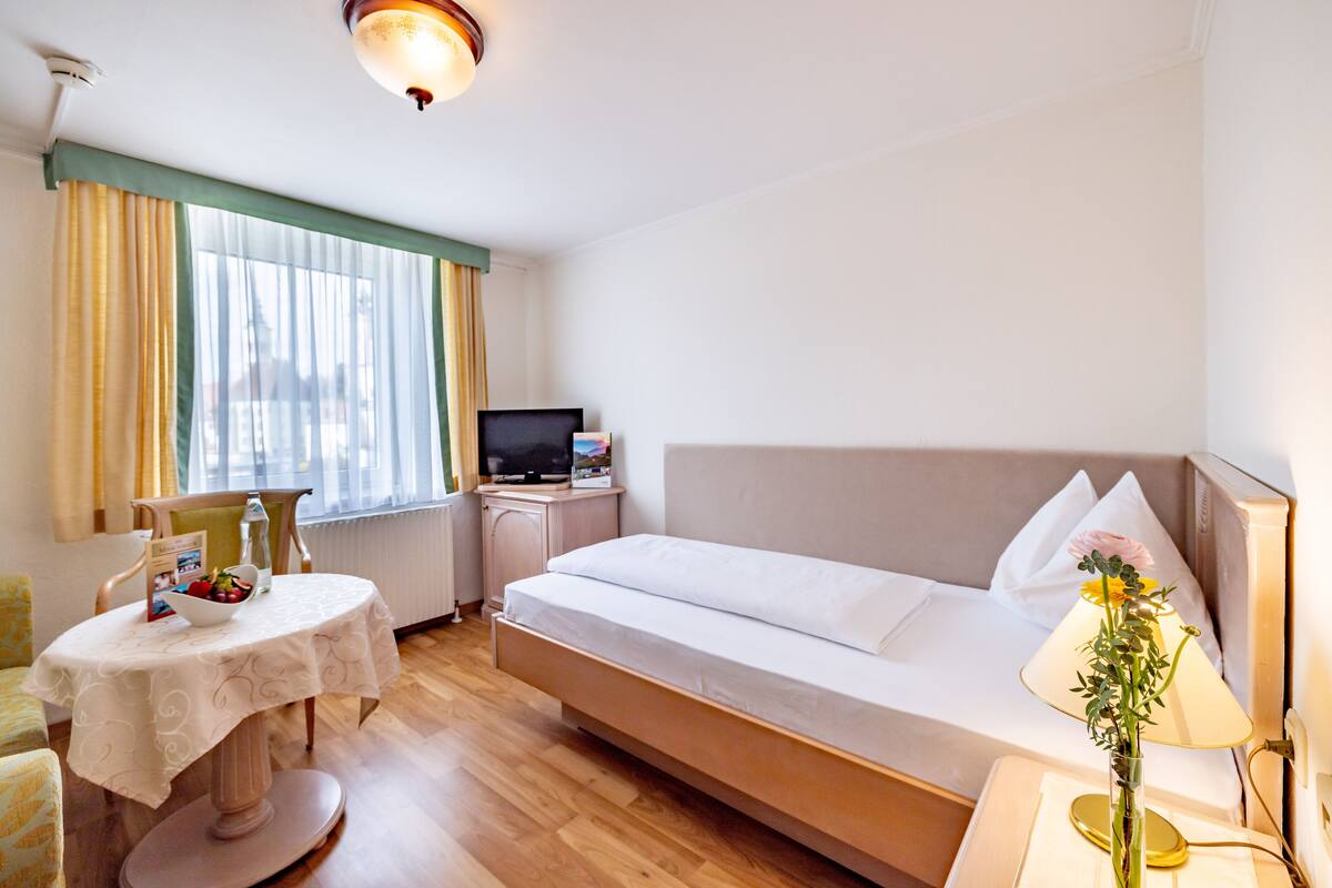 A hotel room with a bed, a table with a bowl of fruit, a television, and a lamp.