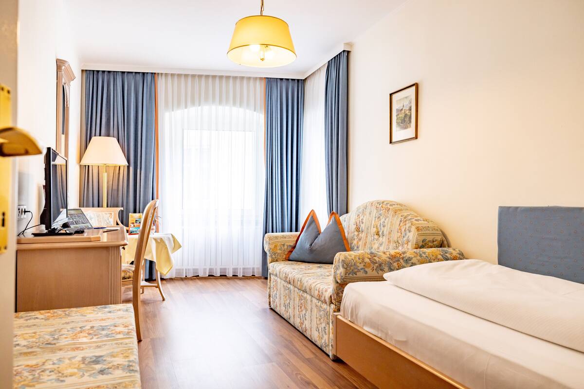 A hotel room with a sofa, a bed, a desk with a lamp, and a chair.