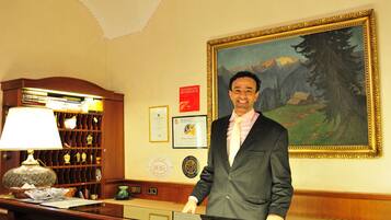 A man standing at a reception desk in a hotel lobby with a painting and framed certificates on the wall.