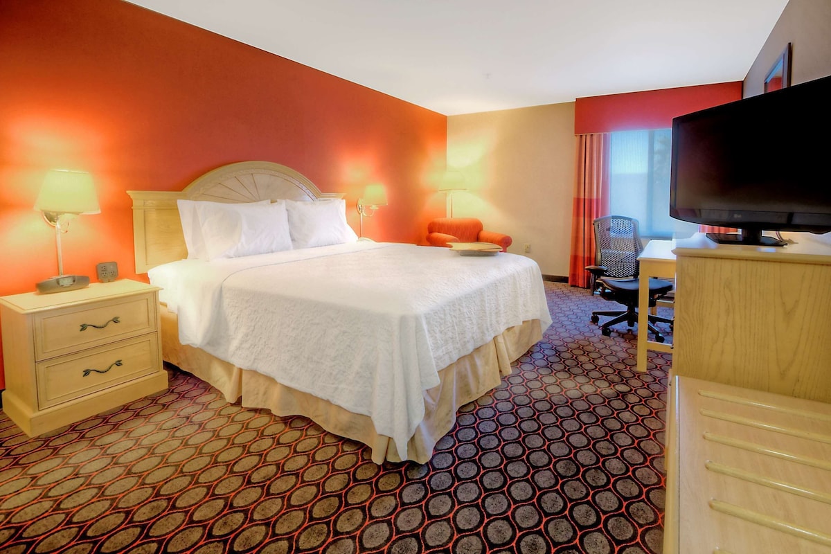 A hotel room with a bed, bedside lamps, a desk with a chair, and a television.