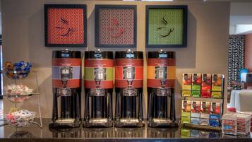 A coffee station with four espresso machines, a selection of tea bags, and a display of bottled water.