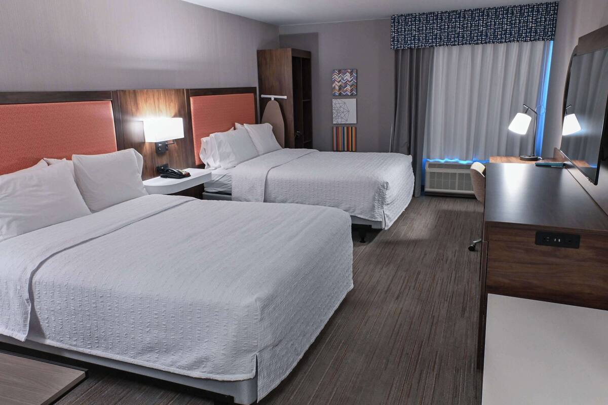 A hotel room with two beds, a desk, a chair, a mirror, and a window with curtains.