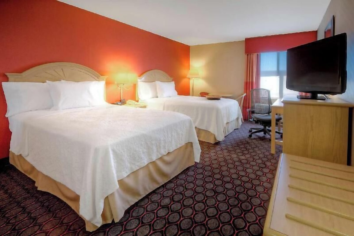 A hotel room with two beds, a TV, a desk, and a chair.