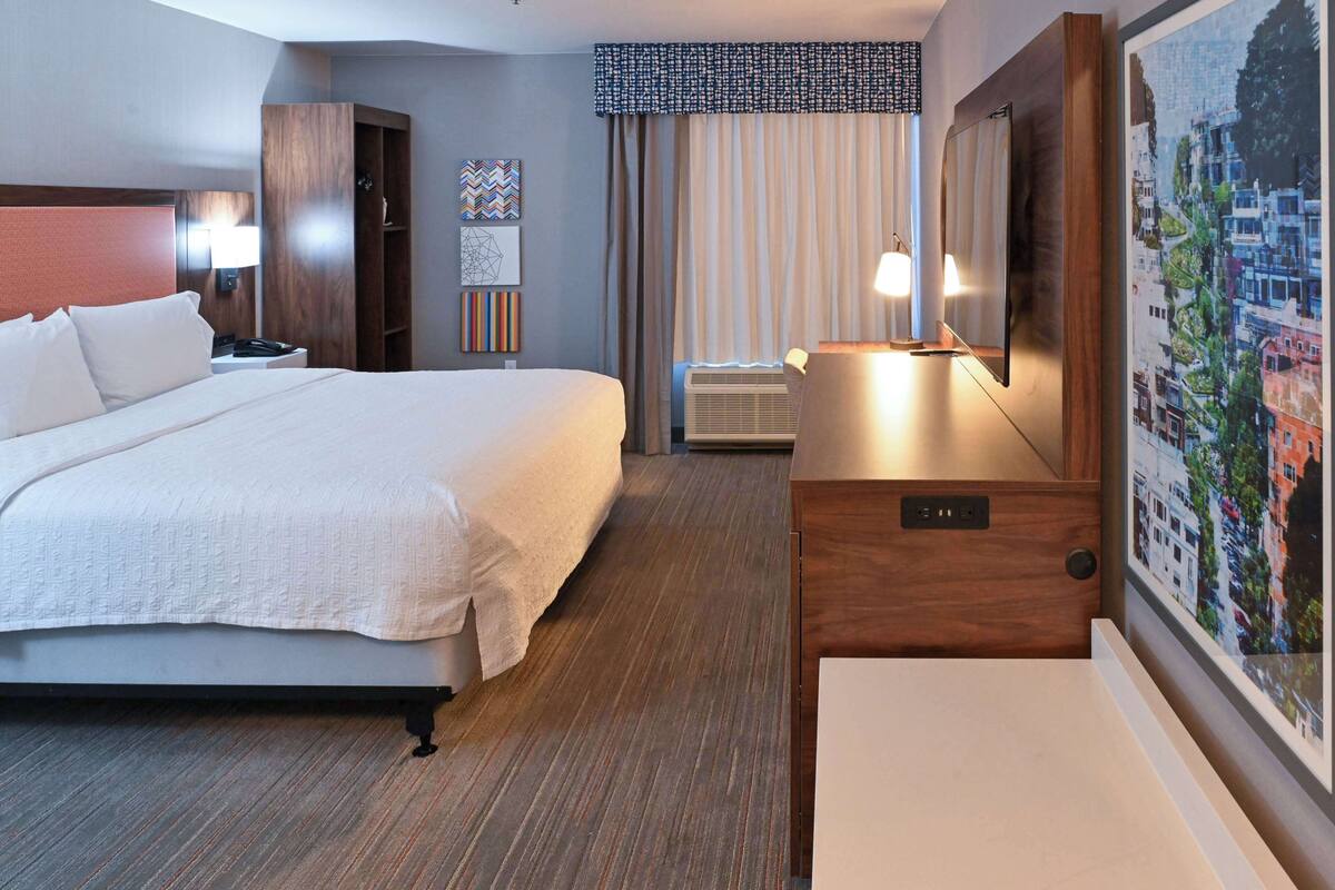 A hotel room with a large bed, a desk, a wardrobe, and a wall-mounted TV.