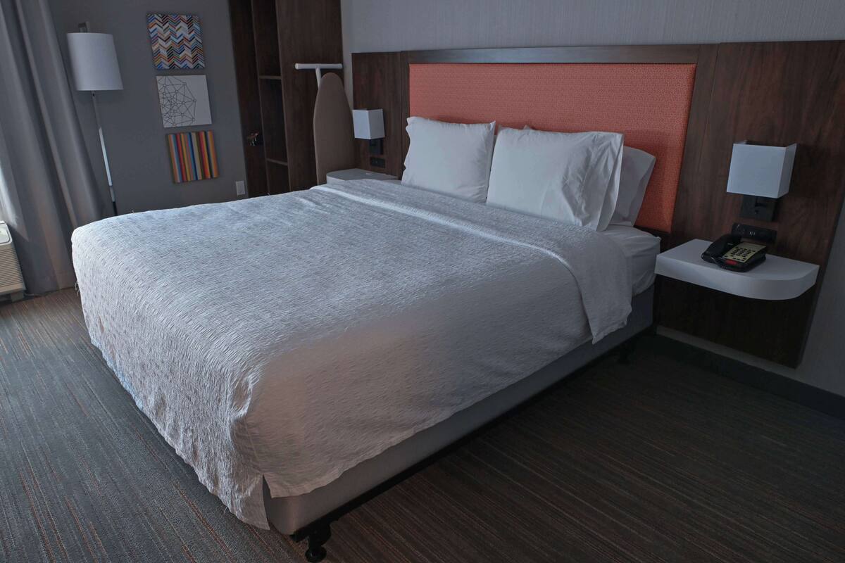A hotel room with a large bed, a nightstand with a phone, and a wall-mounted lamp.