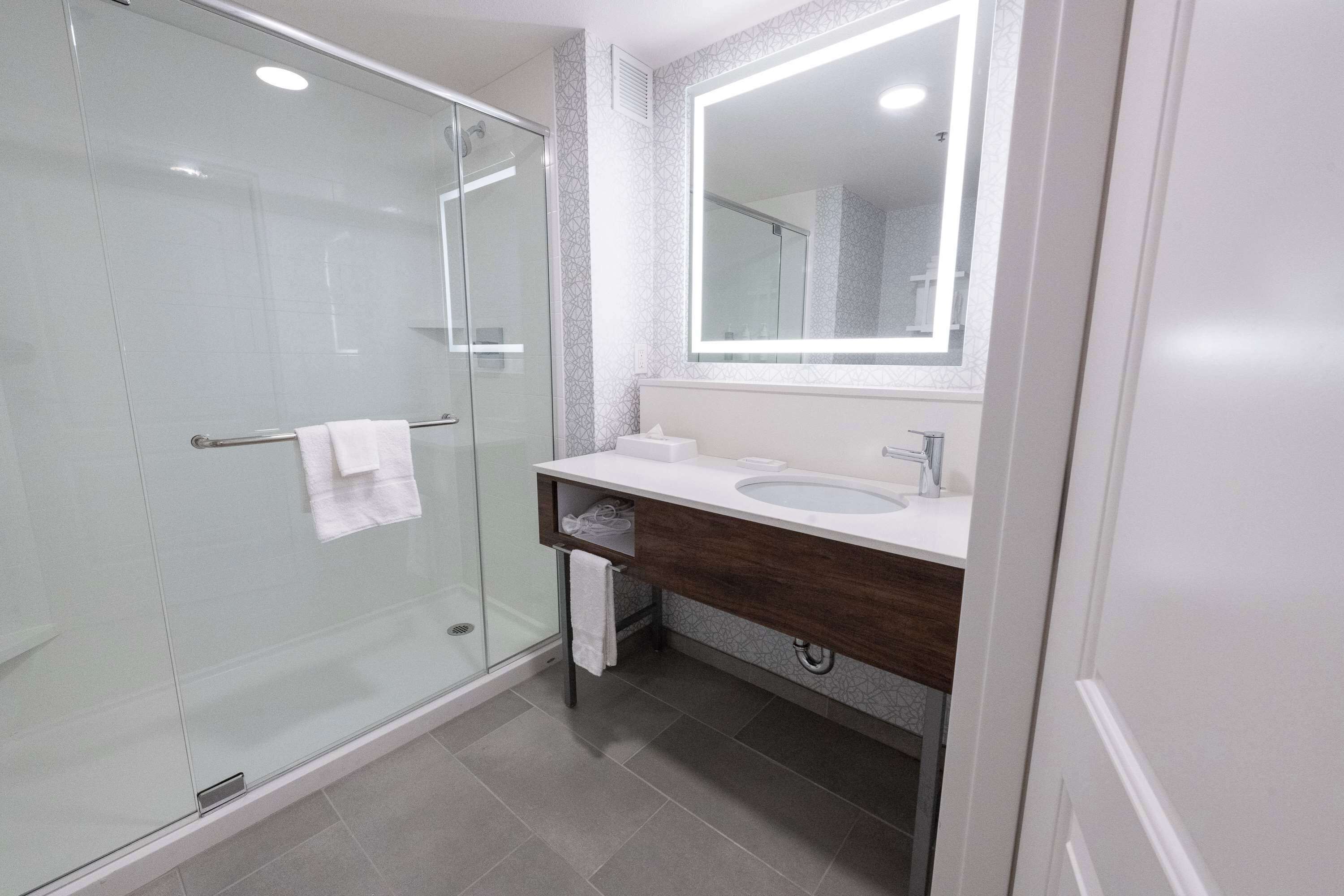 Un bagno moderno con cabina doccia in vetro, un mobile lavabo con specchio e un lavandino.