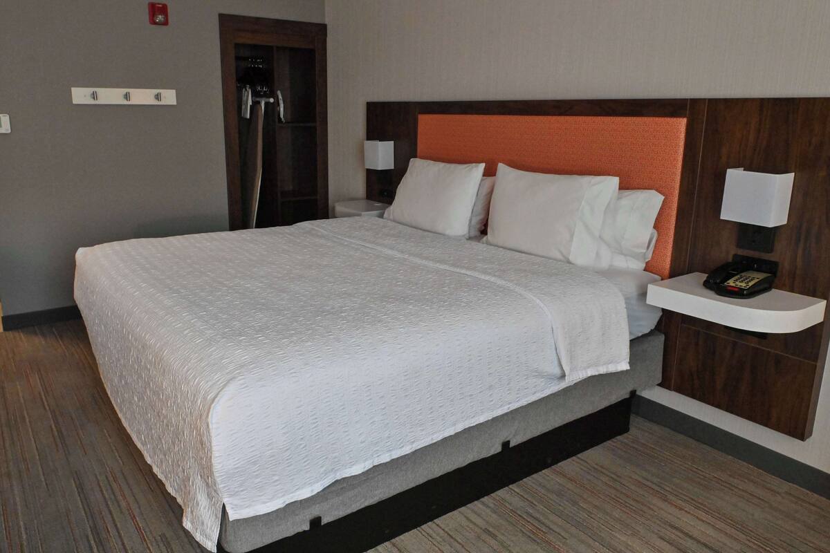 A hotel room with a large bed, a wooden headboard, a nightstand with a phone, and a shower area.