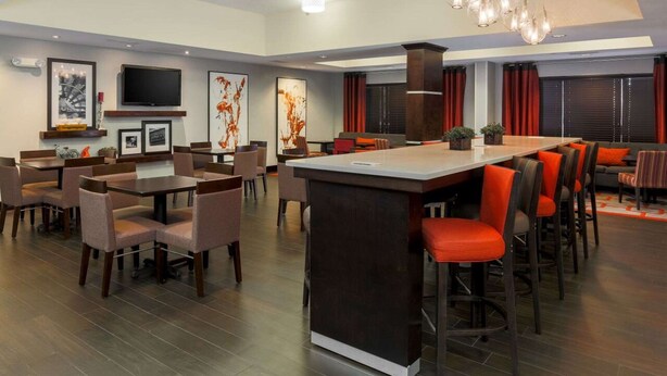A modern dining area with a central bar, multiple seating arrangements, and a large flat-screen TV mounted on the wall. - Hampton Inn Memphis-Southwind (Memphis)