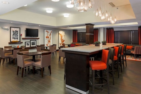 A modern dining area with a central bar, multiple seating arrangements, and a large flat-screen TV mounted on the wall.