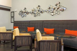 A modern lounge area with a grey sofa, orange cushions, and glass-top tables.