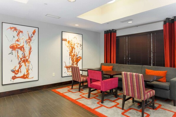 A modern living room with a gray sofa, a dining table with chairs, and two abstract paintings on the wall.