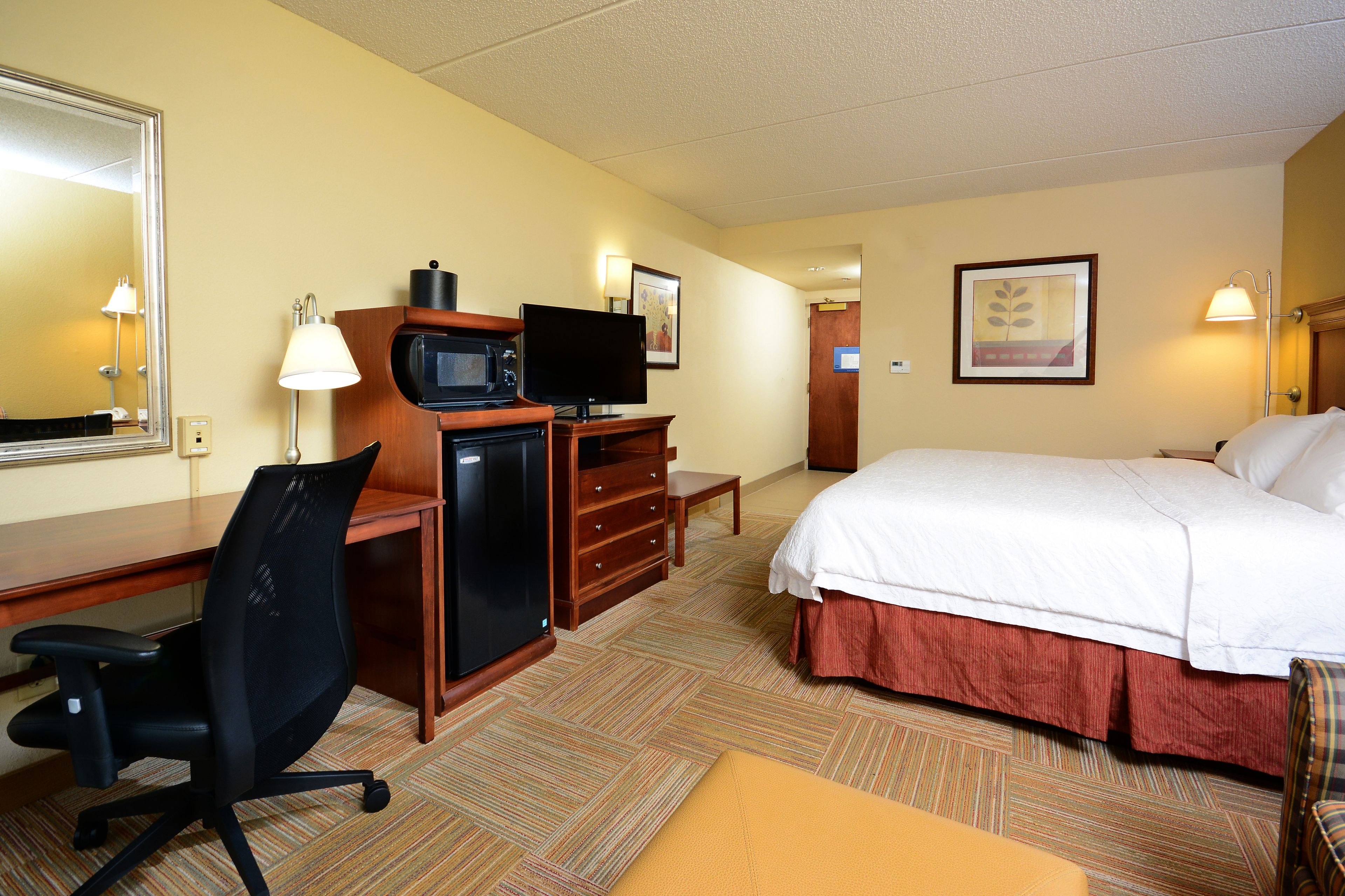 Ein Hotelzimmer mit Bett, Schreibtisch, Stuhl, Fernseher und Mikrowelle.