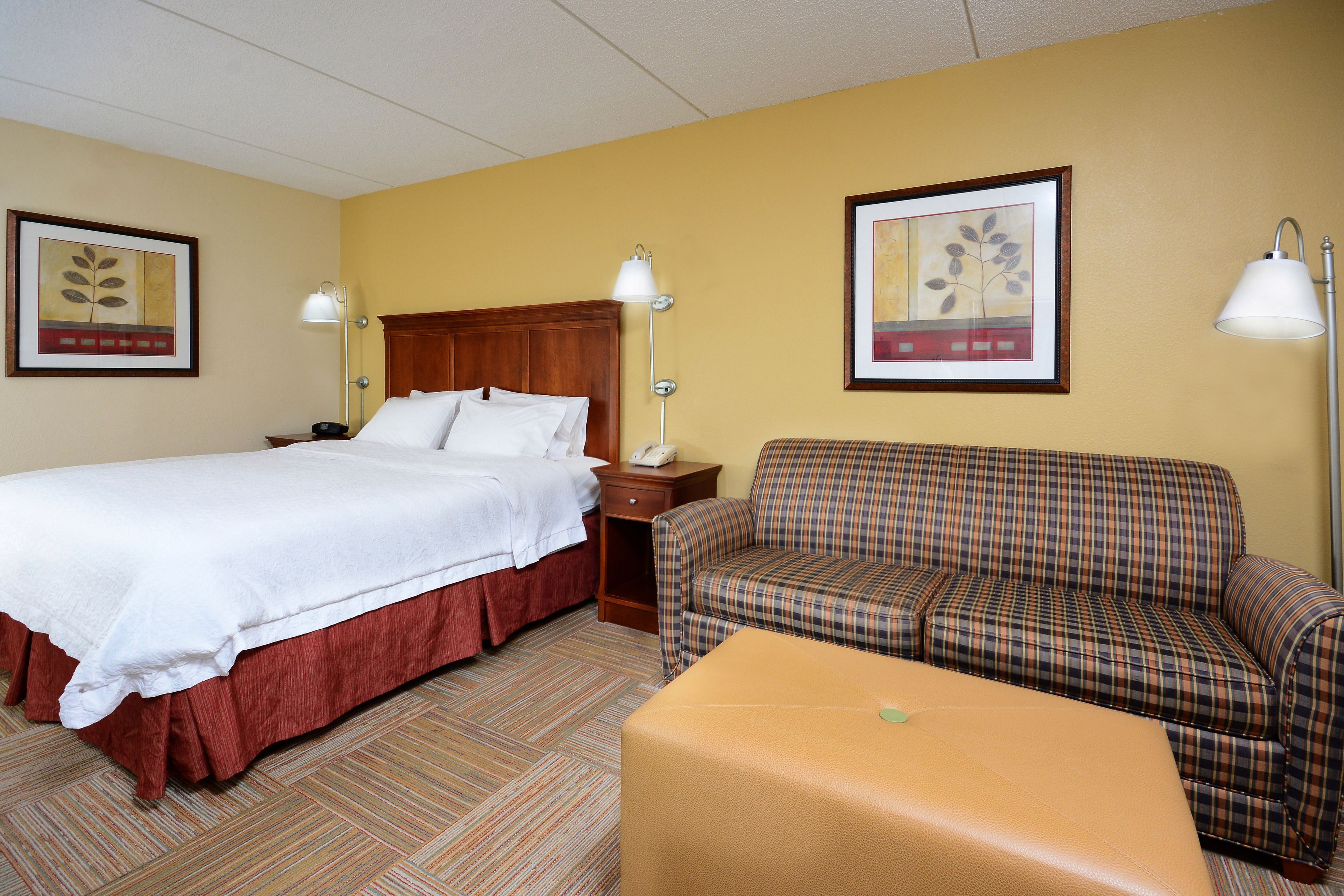 A hotel room with a bed, a sofa, a small table, and two wall-mounted lamps.