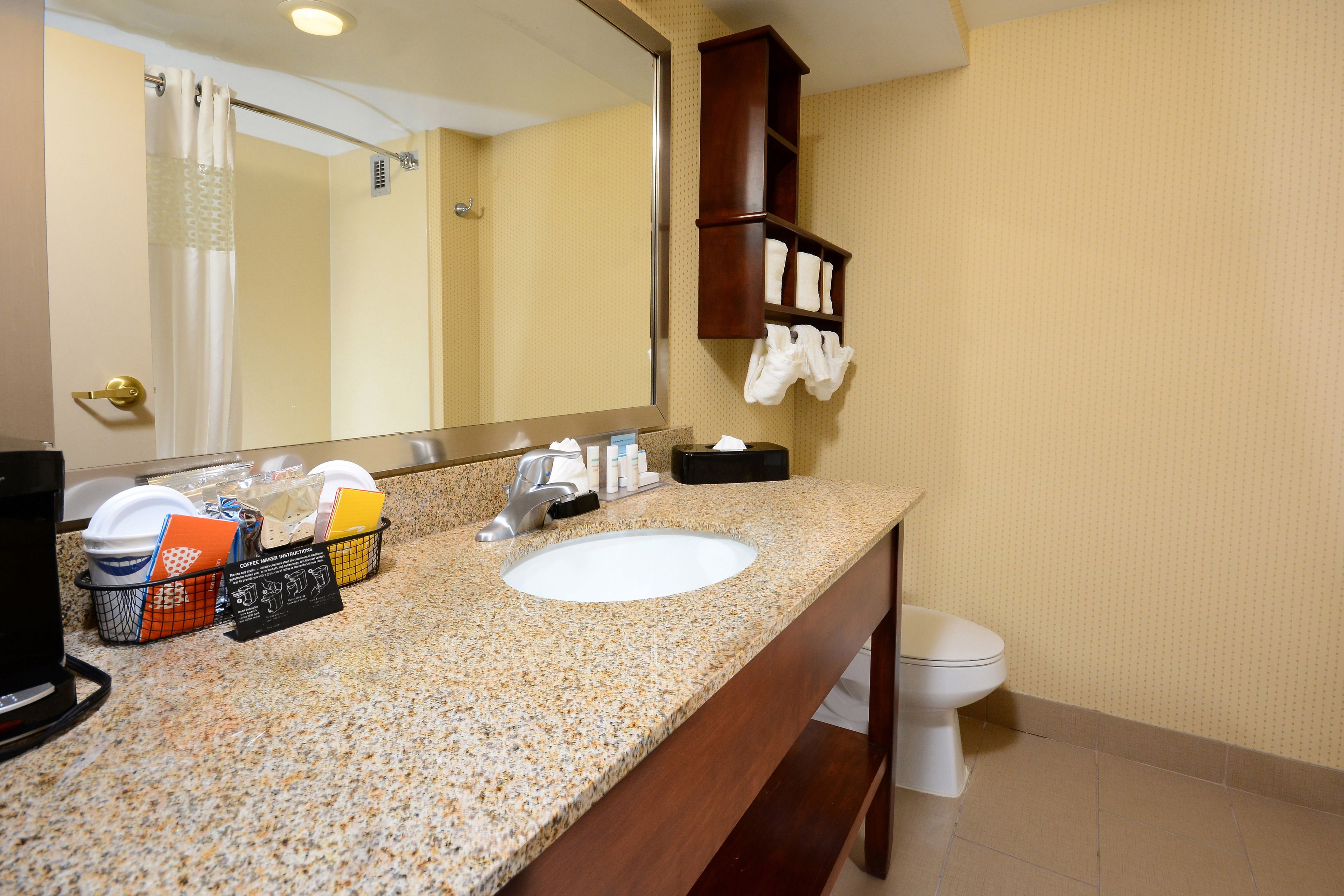Un baño con encimera de granito, lavamanos, espejo, cortina de ducha, toallero y retrete.