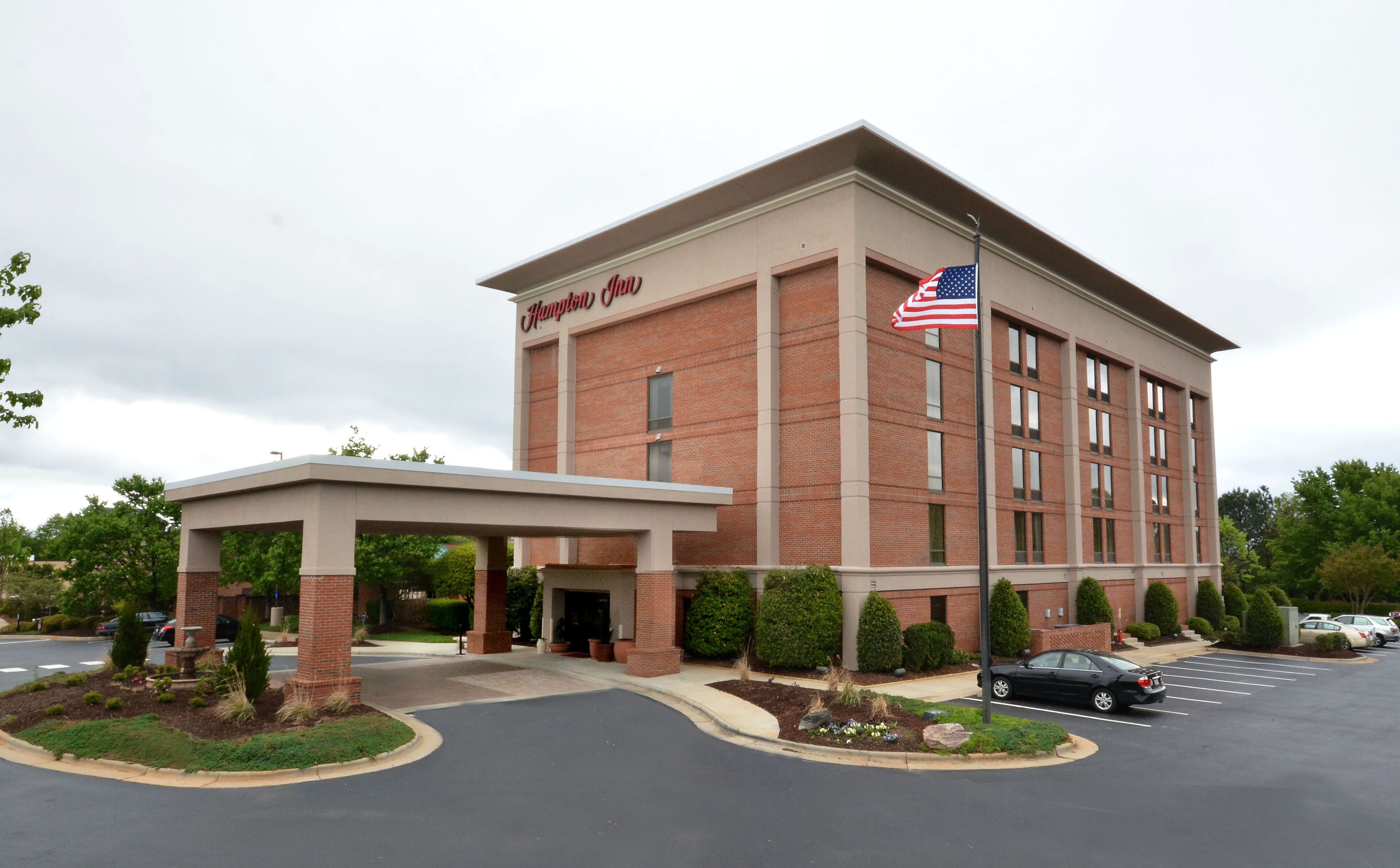 Un hotel Hampton Inn con facciata in mattoni, bandiera americana e ingresso coperto.