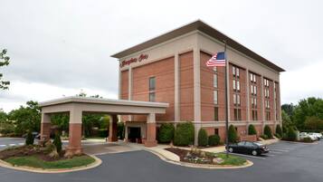 Un hotel Hampton Inn con facciata in mattoni, bandiera americana e ingresso coperto.