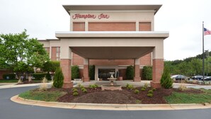 Un hôtel Hampton Inn avec une façade en briques, une entrée abritée et un parterre aménagé avec une fontaine.