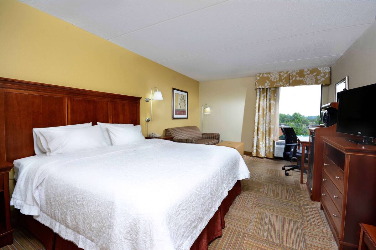 A hotel room with a large bed, a desk, a chair, a television, and a window with curtains.