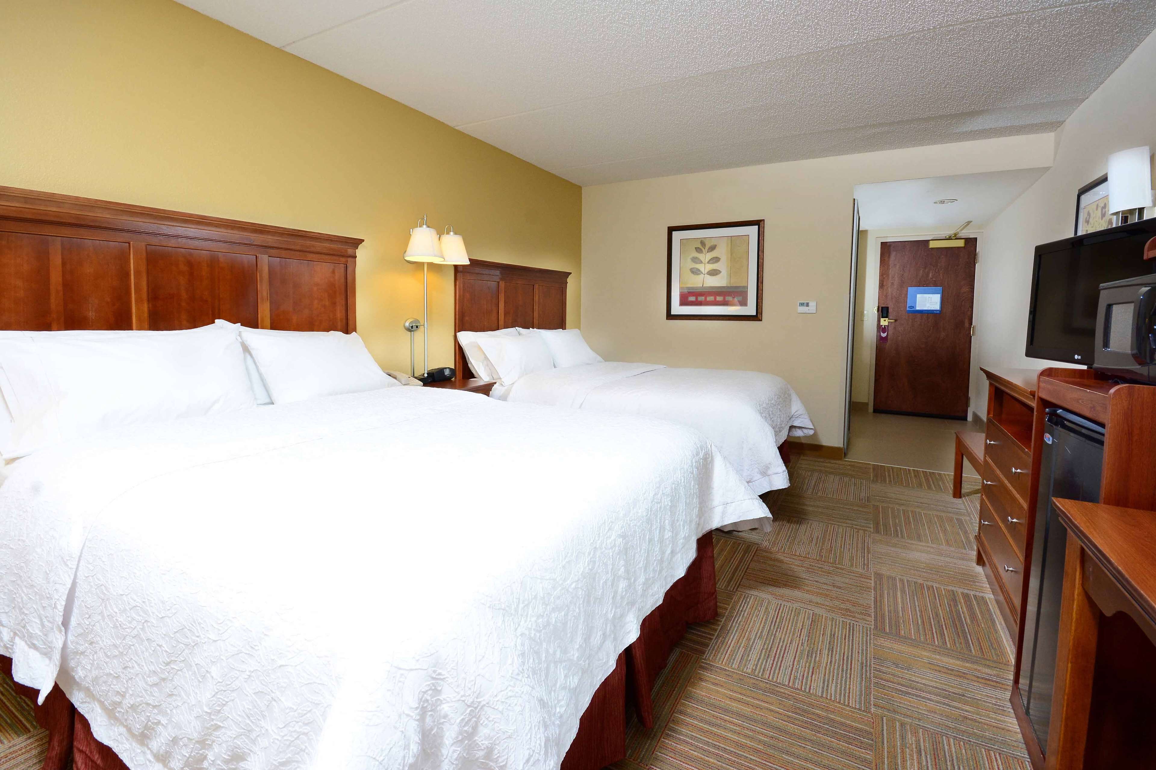 A hotel room with two beds, a television, a desk, and a door leading to a bathroom.