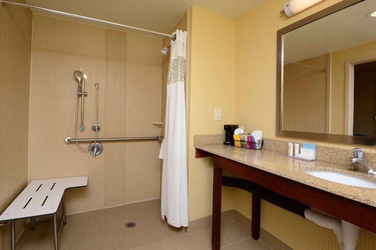 A bathroom with a shower, grab bar, sink, and mirror.