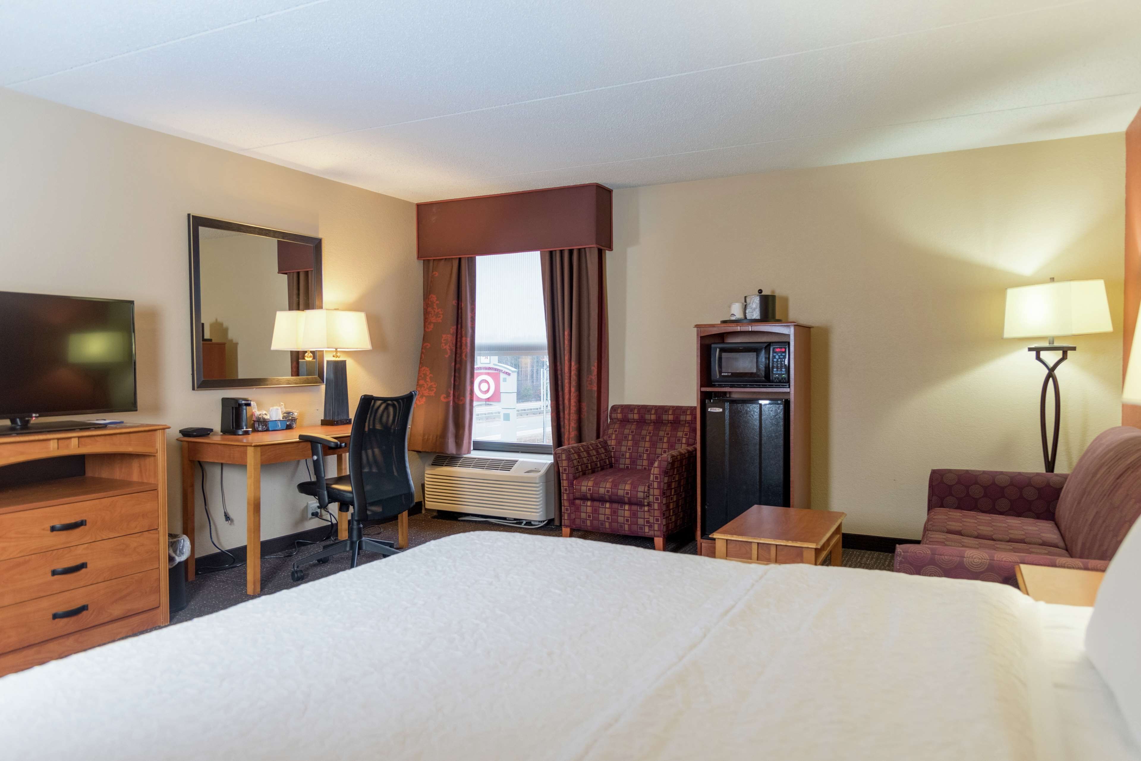 A hotel room with a bed, desk, chair, television, and a small table.